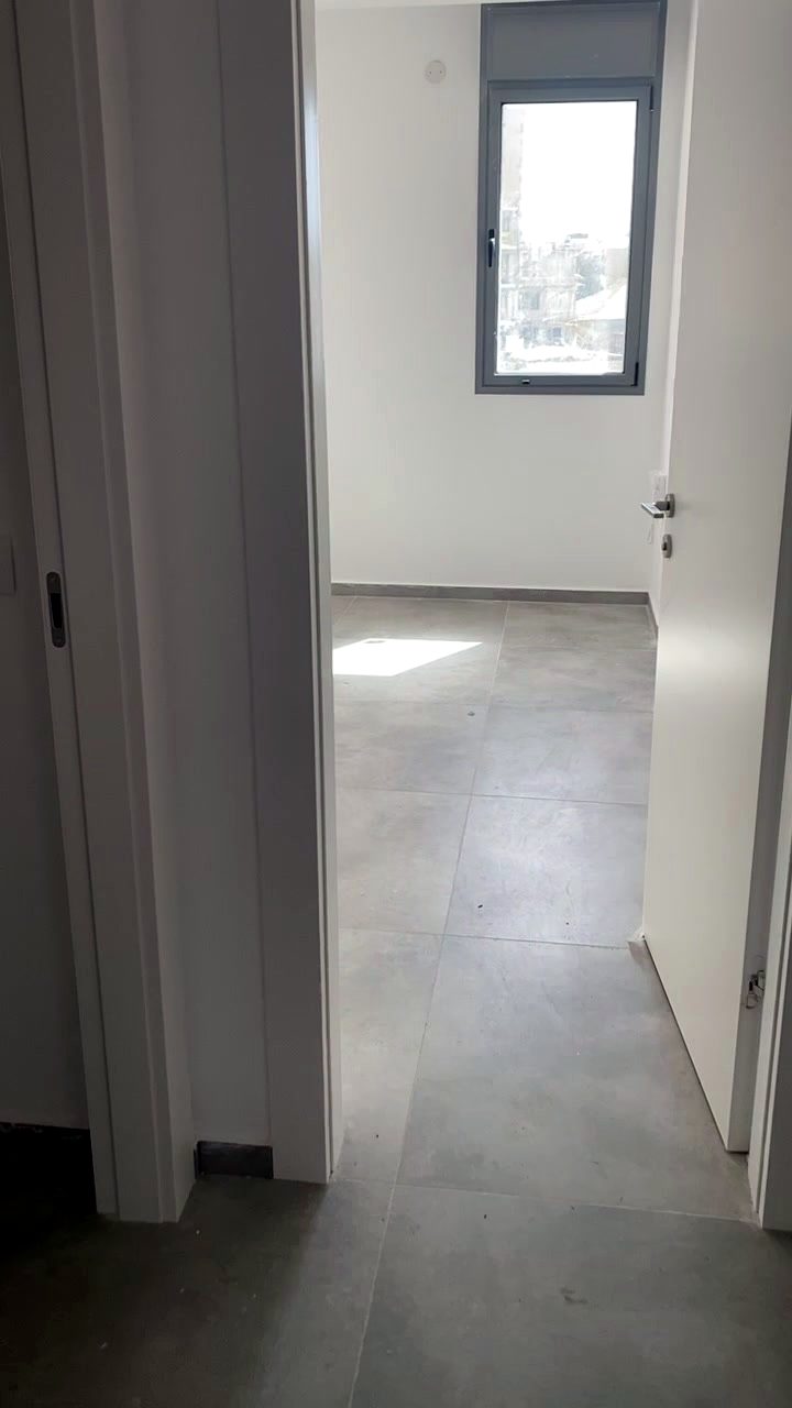 מסדרון ודירה עם ריצוף אפור גדול ודלתות לבנות